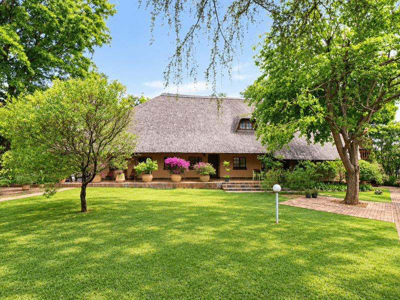 A well-maintained rear garden view featuring a traditional thatched roof house with a tiled patio and established landscaping.