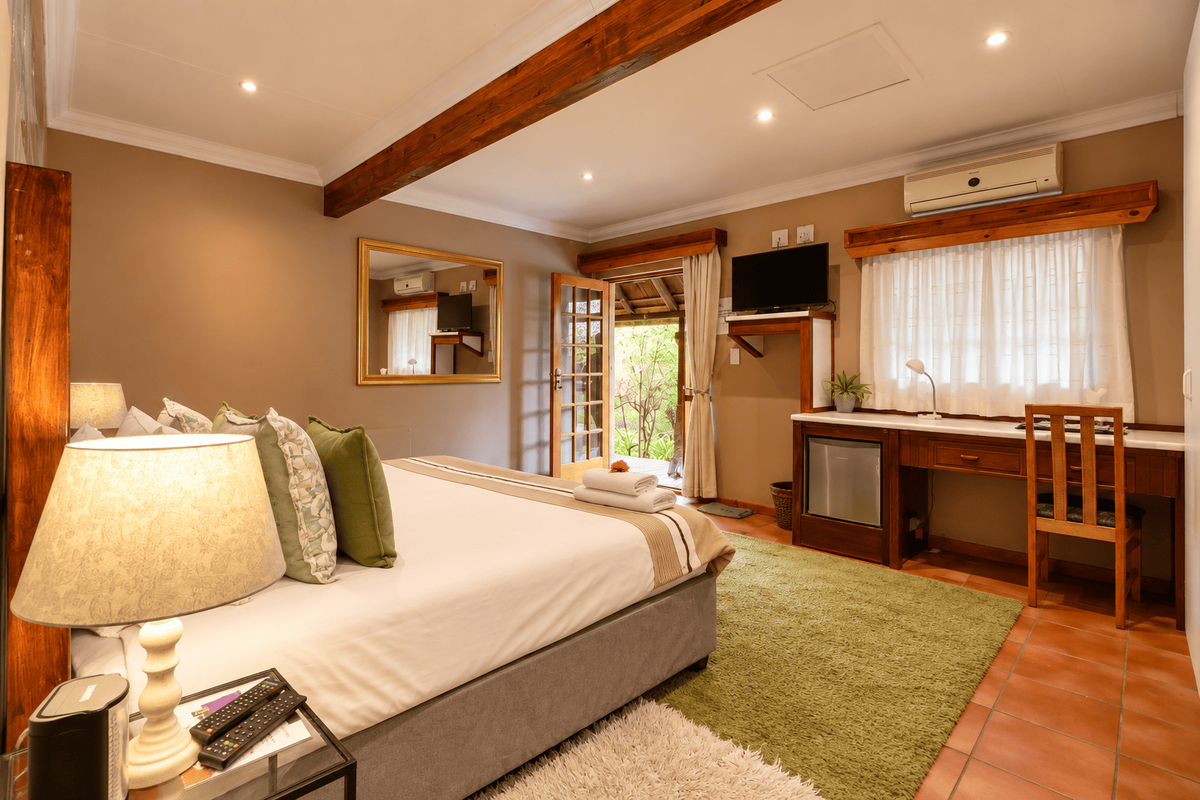 A well-maintained bedroom featuring exposed timber ceiling beams, terracotta flooring, a built-in desk, and direct access to an outdoor area.