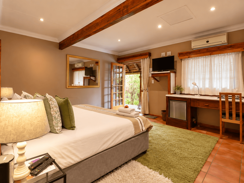 A well-maintained bedroom featuring exposed timber ceiling beams, terracotta flooring, a built-in desk, and direct access to an outdoor area.