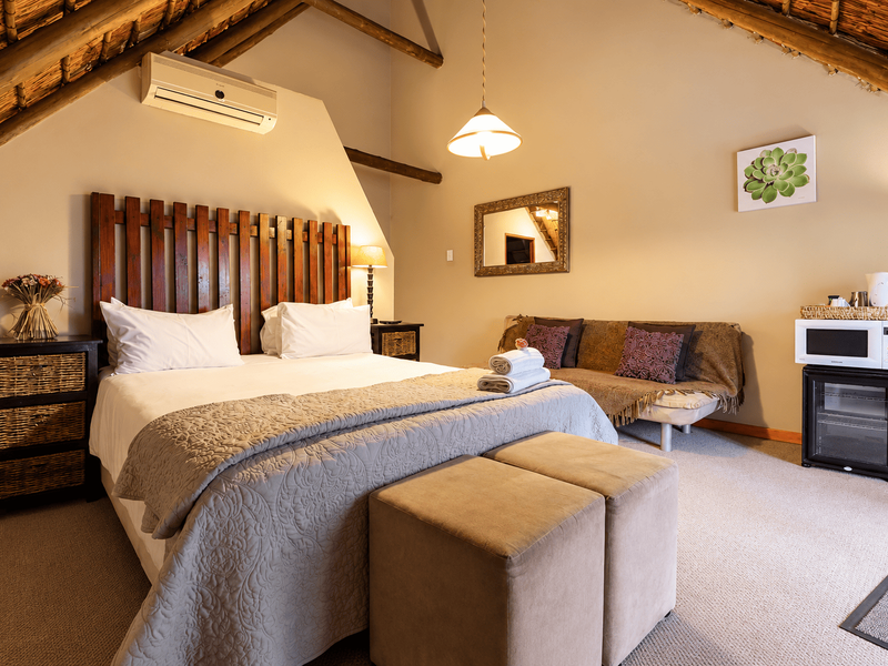 A cozy bedroom featuring a high vaulted ceiling with exposed timber rafters and thatch detailing, complemented by a wall-mounted air conditioning unit.