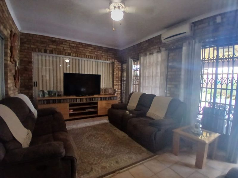 A living room featuring exposed brick walls, tiled flooring, a ceiling fan, and a wall-mounted air conditioning unit with access to an outdoor area.
