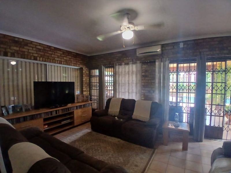 A living room featuring exposed brick walls, tiled flooring, a ceiling fan, and split-system air conditioning, with direct access to an outdoor area.