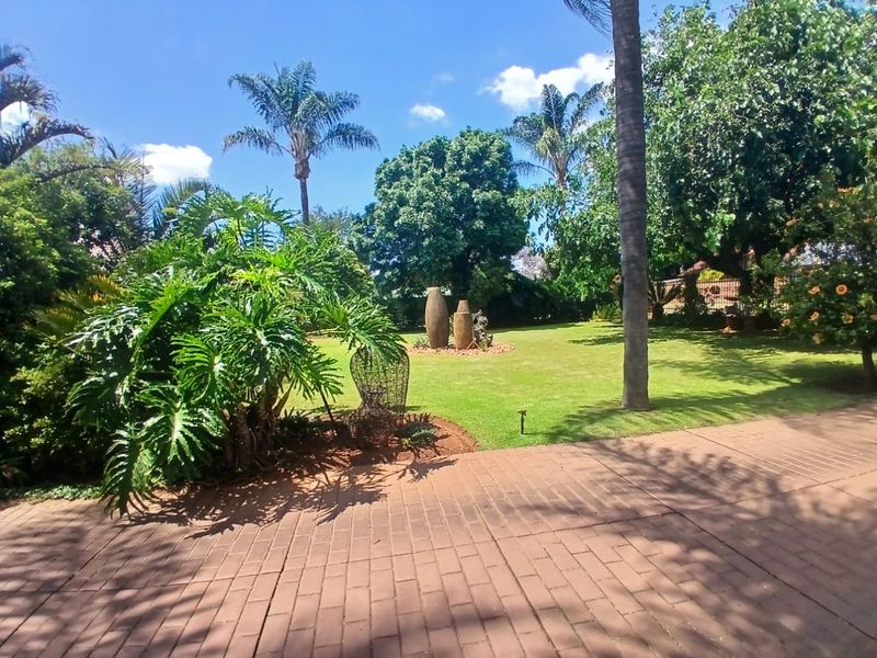 A well-maintained, spacious garden featuring mature trees, lush green lawn, and brick-paved patio area, offering a serene outdoor environment.
