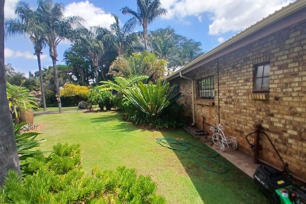 A well-maintained rear garden featuring a face brick exterior wall, established trees, and lush lawn area.