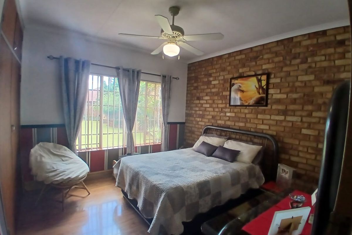 A bedroom featuring an exposed brick feature wall, laminate flooring, built-in cupboards, and a ceiling fan, with security bars on the windows.