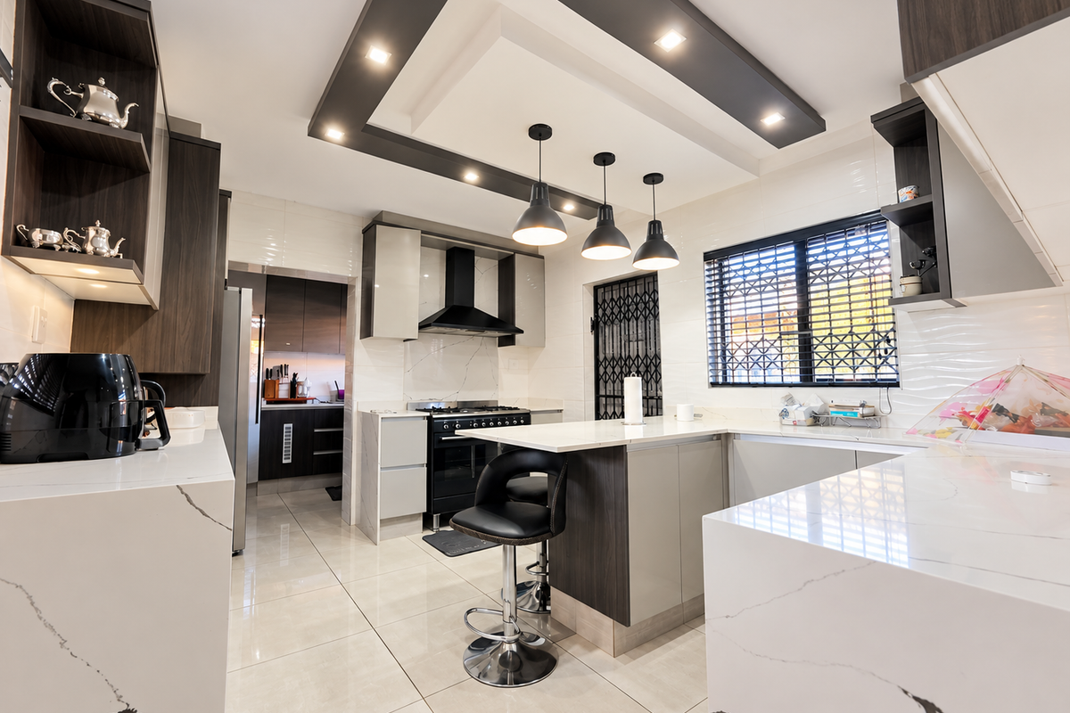 Modern kitchen featuring high-end quartz countertops, sleek cabinetry, built-in oven with extractor fan, and stylish pendant lighting over a central breakfast bar.