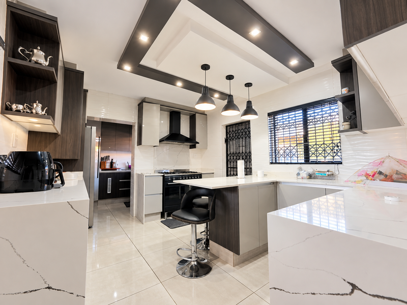 Modern kitchen featuring high-end quartz countertops, sleek cabinetry, built-in oven with extractor fan, and stylish pendant lighting over a central breakfast bar.