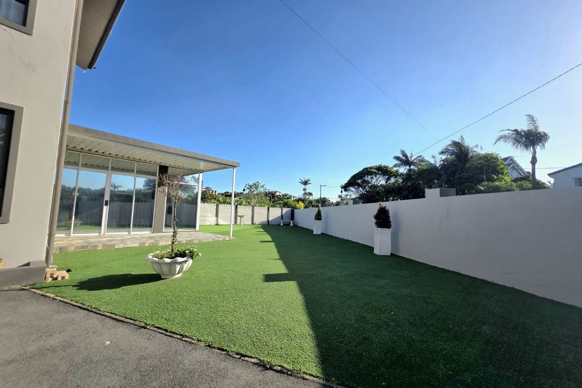 A well-maintained rear garden featuring artificial turf, a high boundary wall, and a covered patio area with large sliding glass doors.