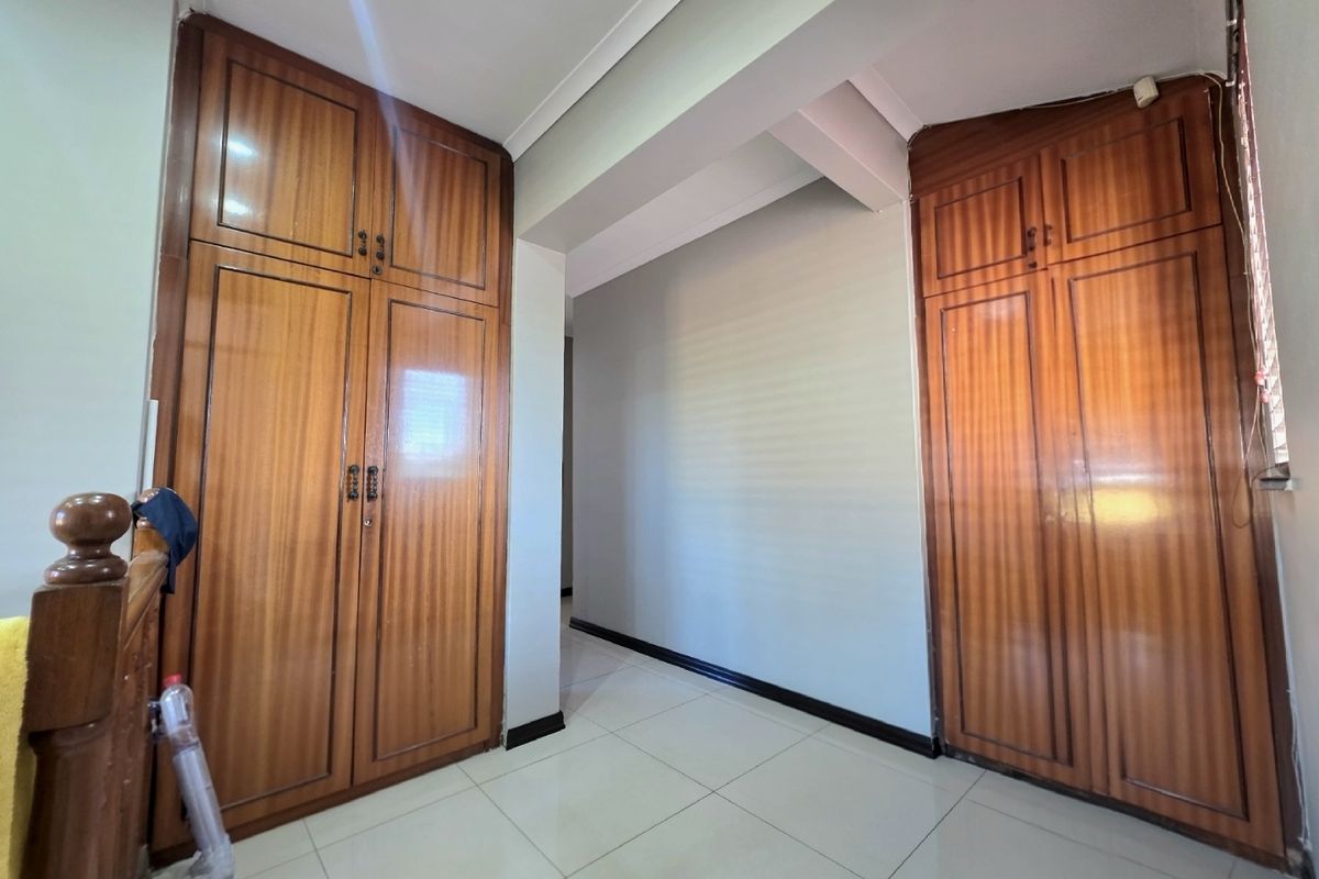 A bedroom featuring built-in wooden cupboards and neutral tiled flooring, offering a clean and functional space ready for personalization.
