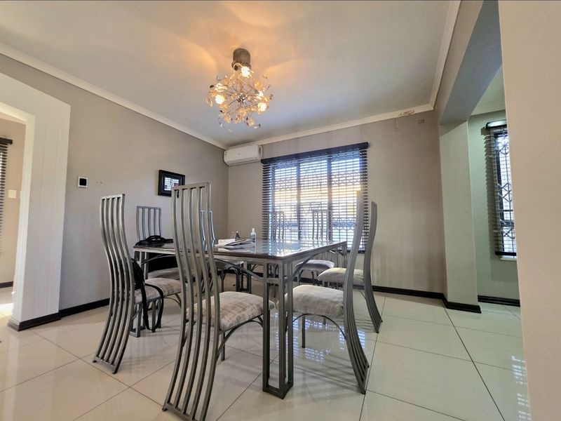A well-maintained dining room featuring large floor tiles, a split-system air conditioner, and modern lighting, providing a bright and functional space for meals.