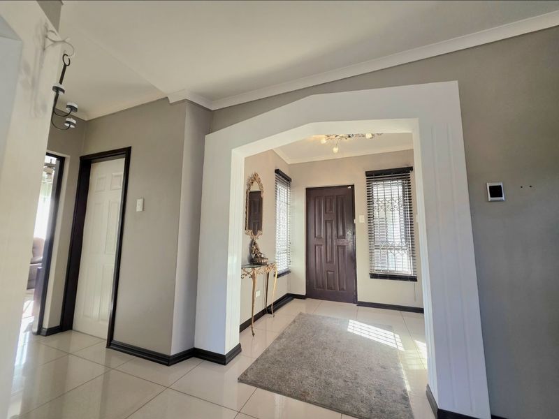 A bright and welcoming entrance hall featuring tiled flooring, a decorative archway, and a secure front door with window blinds.