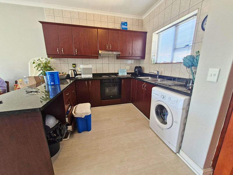 A functional kitchen featuring dark wood cabinetry, granite countertops, a built-in oven with hob, and an integrated washing machine.