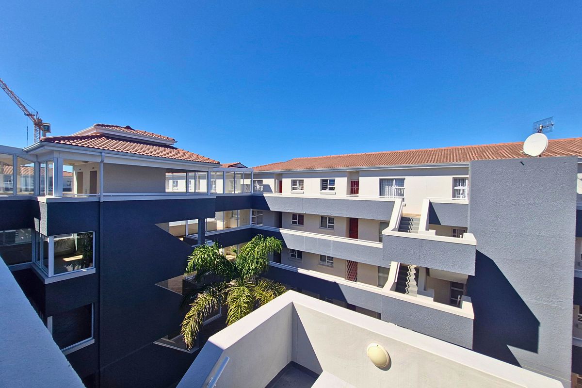 An elevated view of the apartment complex courtyard, featuring modern grey facade finishes, terracotta tiled roofing, and open-air stairwell access.