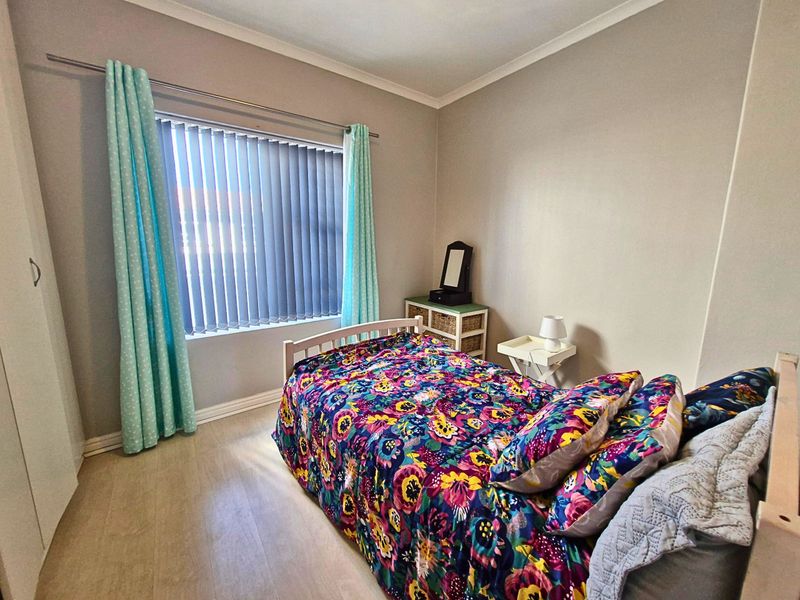 A functional bedroom featuring light-toned laminate flooring, built-in wardrobe storage, and vertical window blinds.