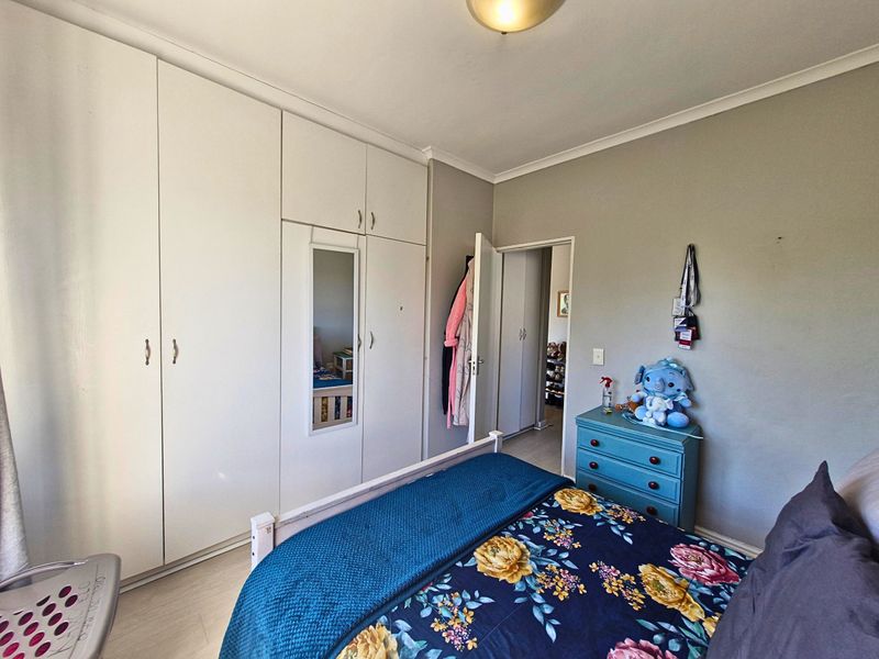 A bedroom featuring floor-to-ceiling built-in cupboards with a central mirror and neutral wall finishes.