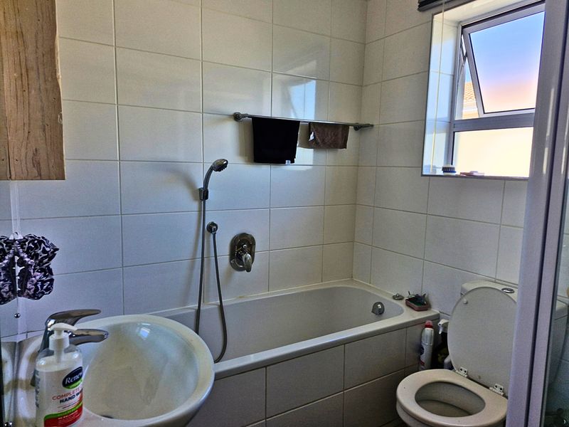 A functional bathroom featuring a bathtub with a handheld shower, a pedestal basin, and a toilet, finished with neutral wall and floor tiling.