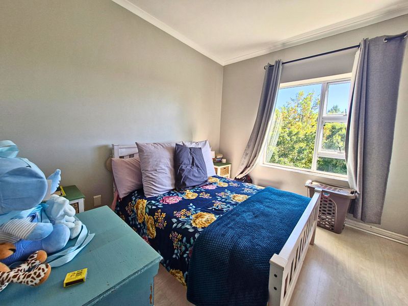 A well-lit bedroom featuring laminate flooring, neutral wall tones, and a large window providing natural light and garden views.