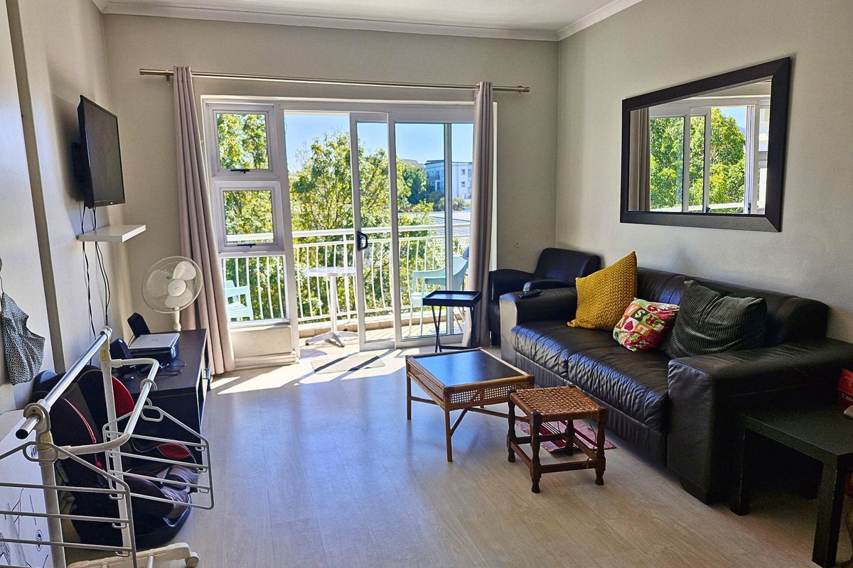 A bright living room featuring laminate flooring and a large sliding glass door that provides direct access to a private balcony.