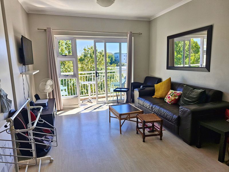 A bright living room featuring laminate flooring and a large sliding glass door that provides direct access to a private balcony.