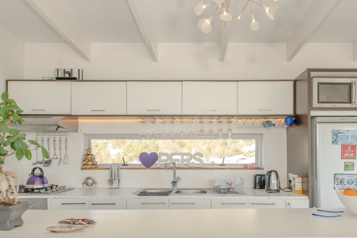 Modern kitchen featuring white cabinetry, exposed ceiling beams, integrated appliances, and a sleek horizontal window providing natural light over the workspace.