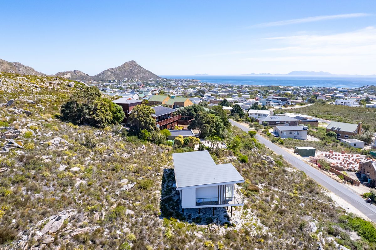 Aerial view of a modern elevated home situated on a hillside, showcasing the surrounding coastal landscape and residential neighborhood.