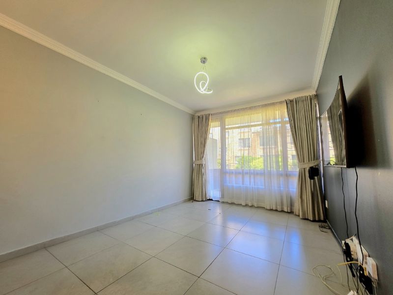 A bright and spacious living room featuring neutral tiled flooring, crown molding, and a large window that allows for ample natural light.