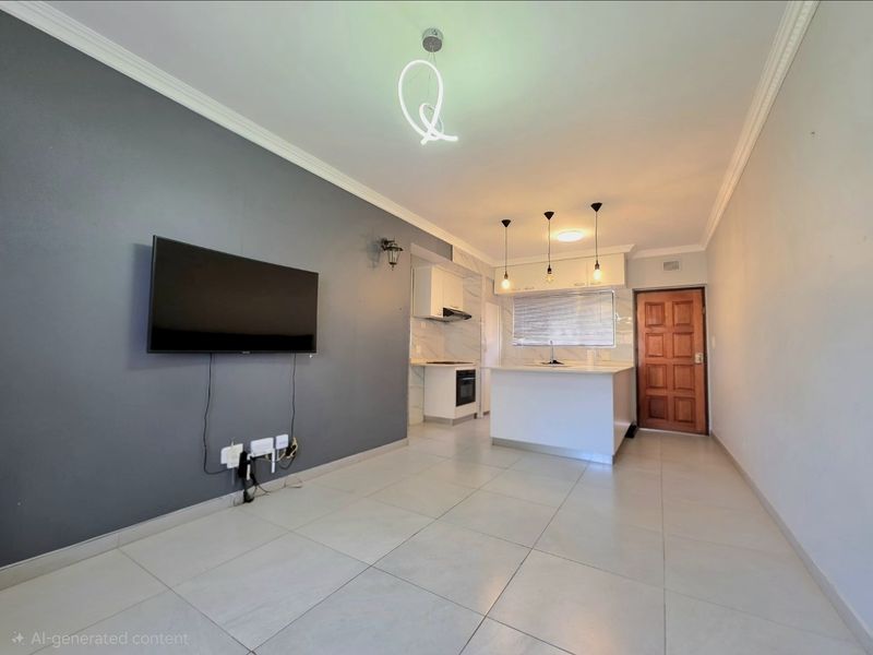 Open-plan living and kitchen area featuring tiled flooring, modern cabinetry, a kitchen island, and a neutral grey feature wall.