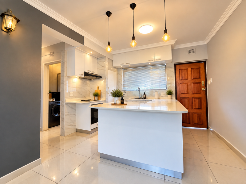 Modern kitchen featuring a central island, sleek white cabinetry, marble-look backsplash, built-in oven, and stylish pendant lighting, with an adjacent laundry area.