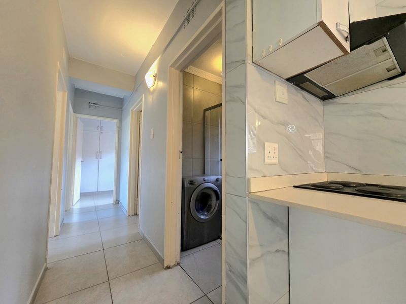 Compact kitchen area featuring built-in cabinetry, electric hob, and extractor fan, leading into a hallway with access to a laundry utility space.