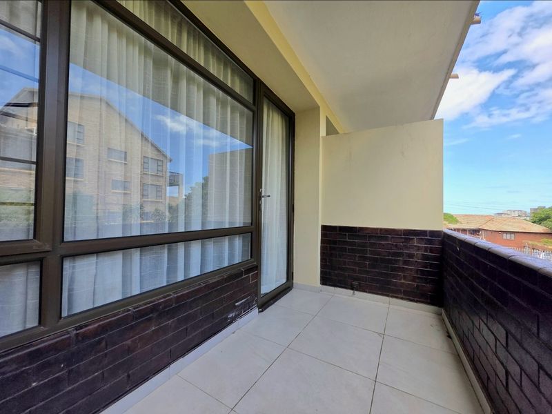 A covered balcony featuring tiled flooring and dark brick wall accents, providing an outdoor space accessible through large aluminium sliding doors.