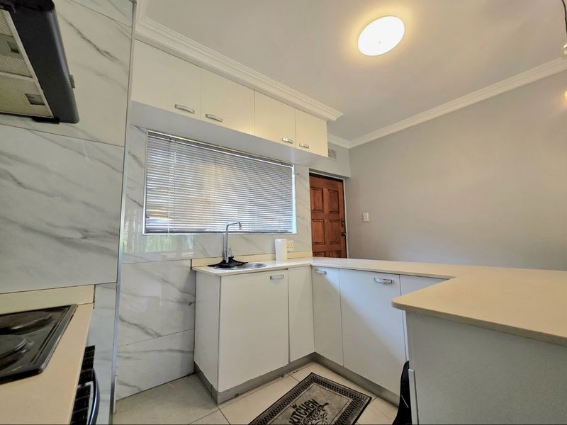 A functional kitchen featuring white cabinetry, marble-look wall tiling, a stainless steel sink, and integrated cooking appliances.