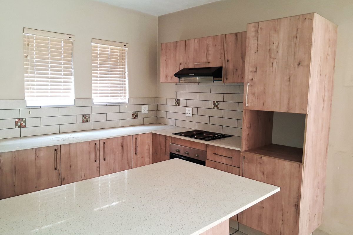 Modern kitchen featuring light wood-look cabinetry, stone countertops, subway tile backsplash, and a functional island with integrated hob and oven.