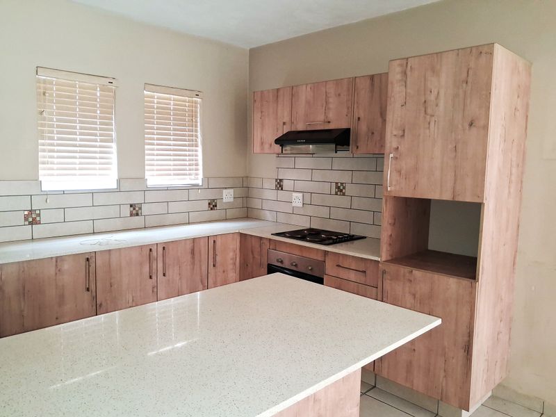 Modern kitchen featuring light wood-look cabinetry, stone countertops, subway tile backsplash, and a functional island with integrated hob and oven.