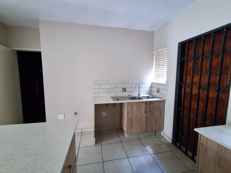 A compact kitchen area featuring built-in cabinetry, a double sink, tiled backsplash, and tiled flooring, with a security gate at the entrance.