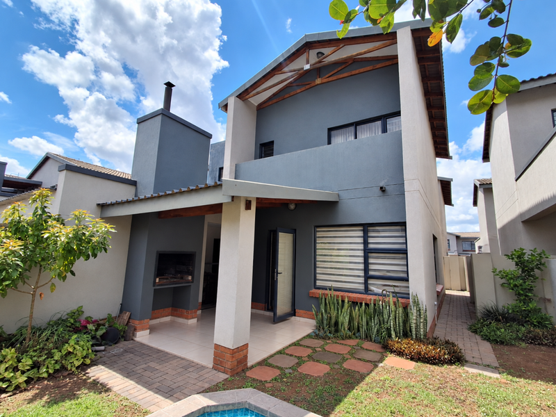 Rear view of a modern townhouse featuring a covered patio with a built-in braai, paved garden area, and a small plunge pool.