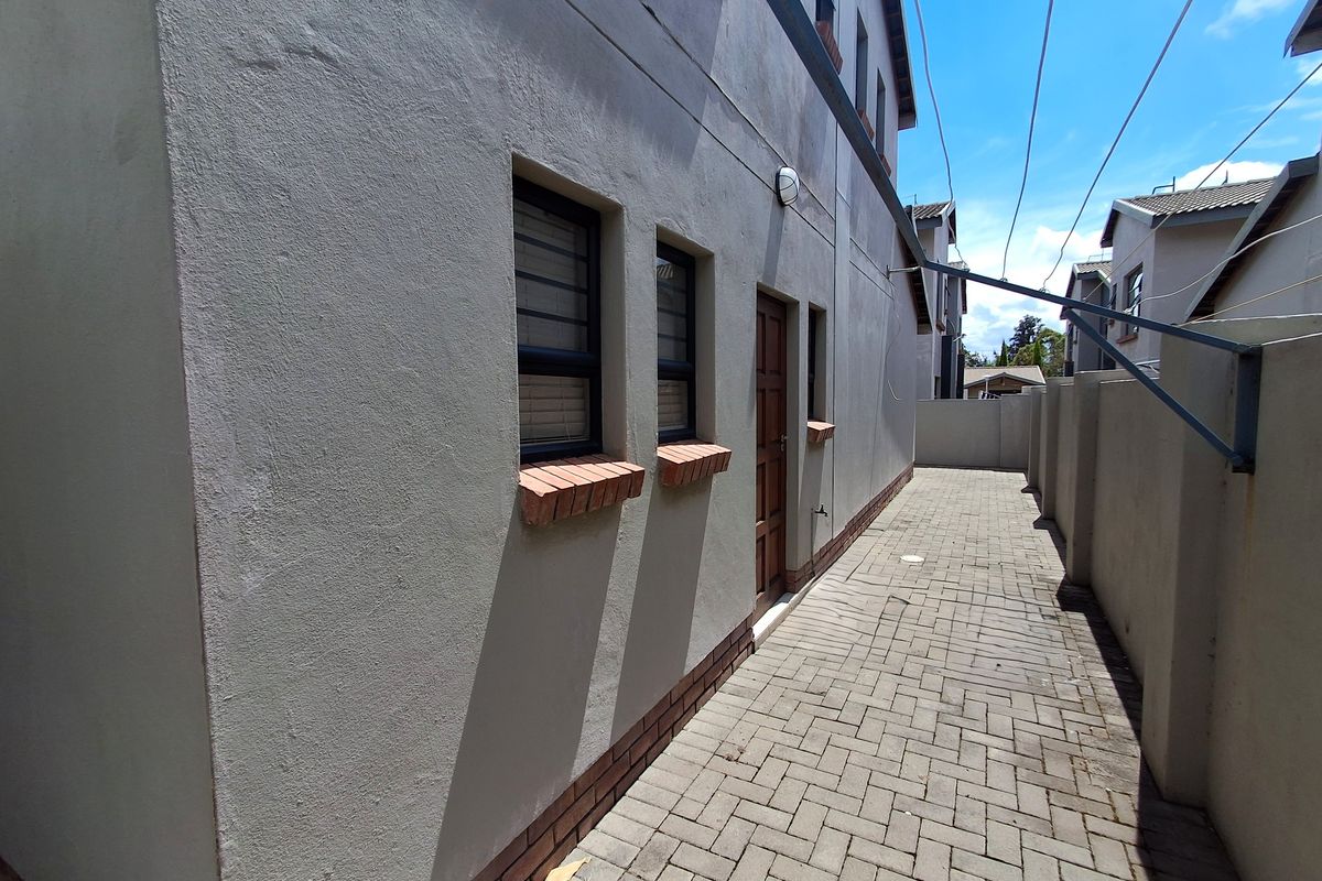 A side exterior view of the townhouse featuring a paved walkway, boundary wall, and external utility access points.