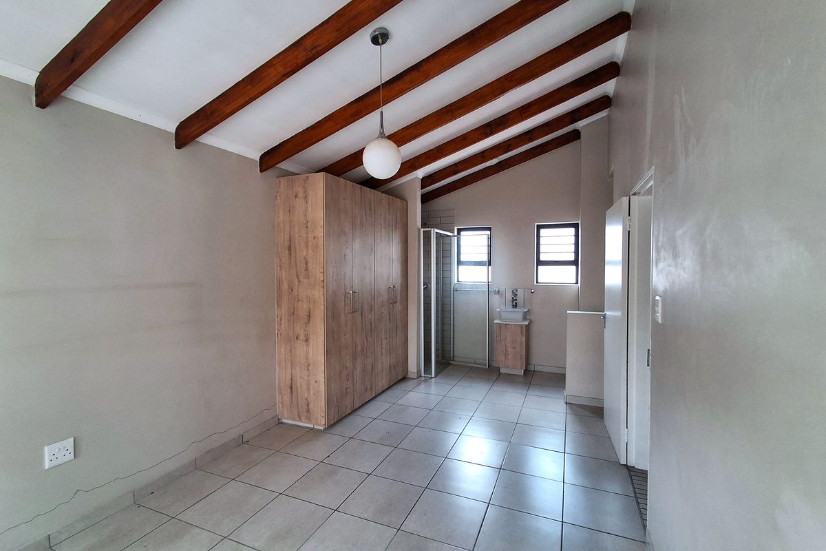 Spacious bedroom featuring exposed timber ceiling beams, tiled flooring, a built-in wardrobe, and an en-suite bathroom with a shower and vanity.