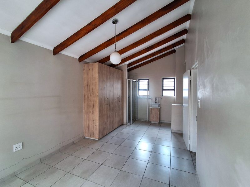 Spacious bedroom featuring exposed timber ceiling beams, tiled flooring, a built-in wardrobe, and an en-suite bathroom with a shower and vanity.
