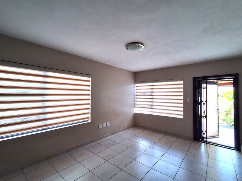 A bright, empty living room featuring neutral wall tones, tiled flooring, modern zebra blinds, and a secure entrance door.