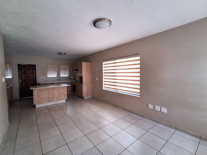 Open-plan living area featuring tiled flooring, a modern kitchen with built-in cabinetry, an island, and integrated appliances, complemented by neutral wall finishes.