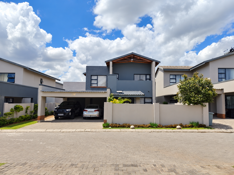 Front elevation of a modern townhouse featuring a double carport, paved driveway, and contemporary grey facade with exposed timber roof detailing.