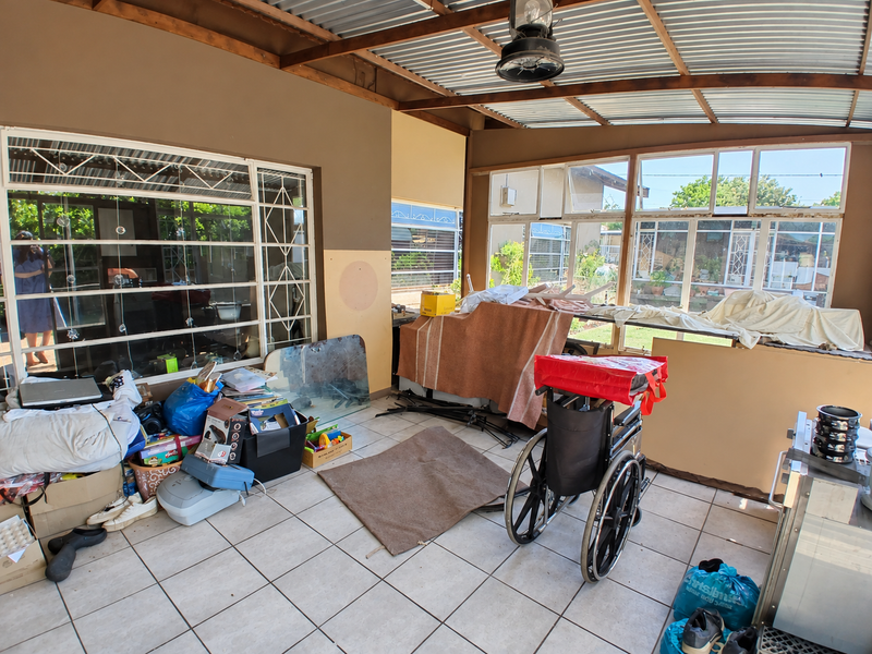 A covered patio area featuring tiled flooring, timber roof beams, and large windows, offering a versatile outdoor space with potential for renovation.