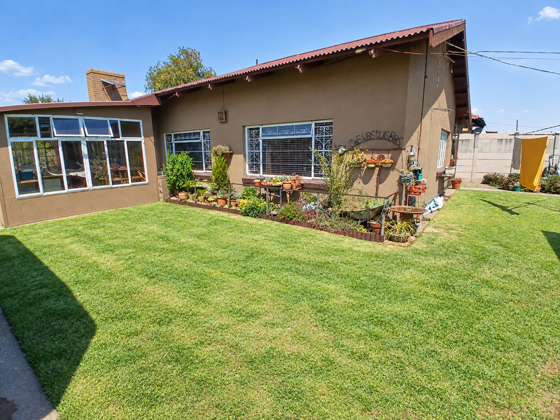 Rear view of the house featuring a well-maintained lawn, an enclosed sunroom, and a brick chimney, set against a secure boundary wall.
