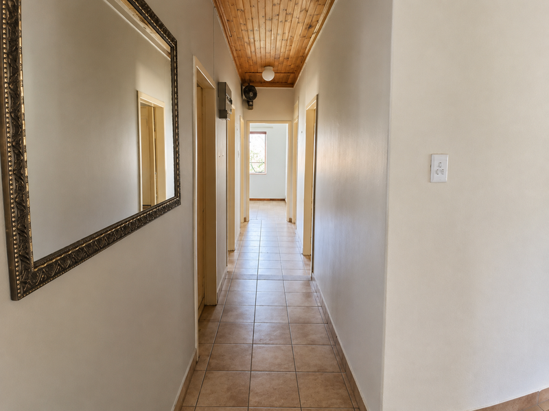 A clean, tiled hallway featuring a warm timber-paneled ceiling and neutral walls, providing access to multiple rooms within the home.