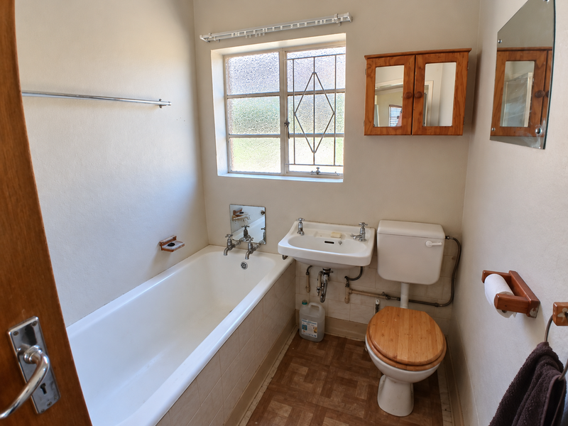 A functional bathroom featuring a bathtub, wall-mounted basin, and toilet, with dated finishes and fixtures ready for a modern update.