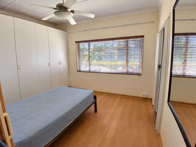 A functional bedroom featuring built-in cupboards, laminate flooring, a ceiling fan, and venetian blinds, offering a clean and practical living space.