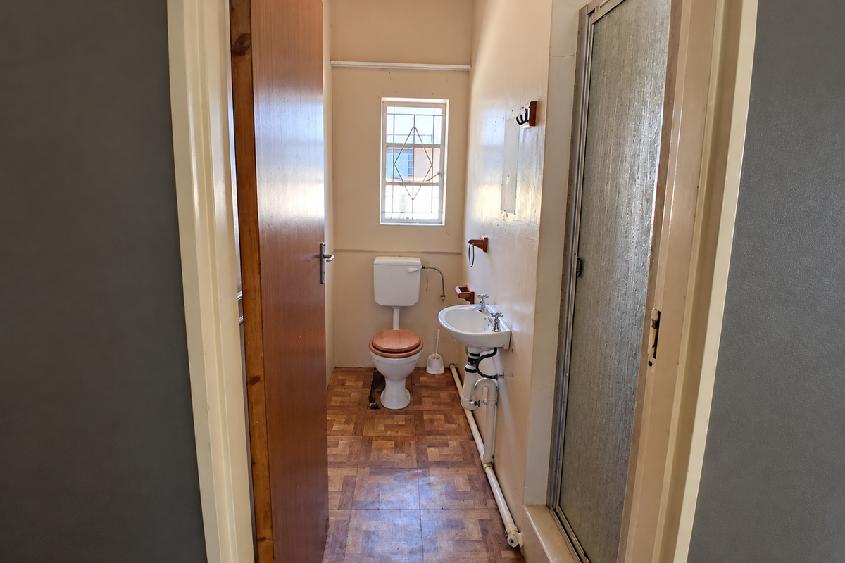 A compact bathroom featuring a toilet, wall-mounted washbasin, and a shower enclosure with dated finishes and exposed plumbing.
