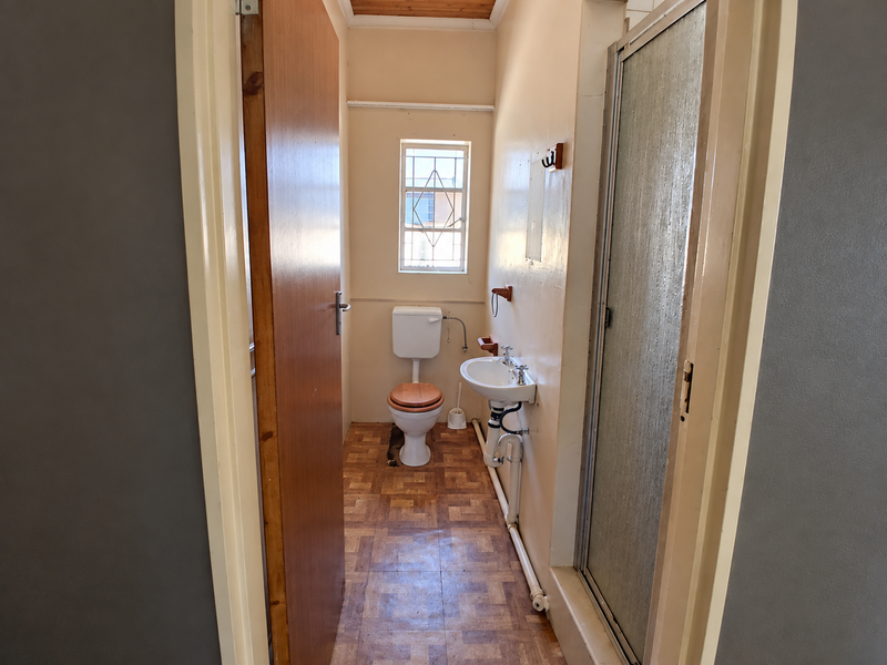 A compact bathroom featuring a toilet, wall-mounted washbasin, and a shower enclosure with dated finishes and exposed plumbing.