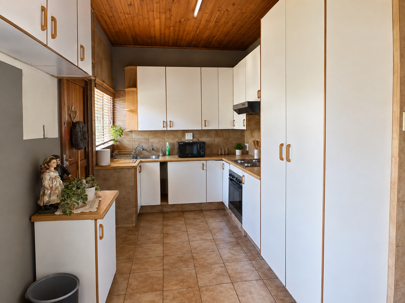 Functional kitchen featuring white cabinetry, laminate countertops, built-in oven and hob, tiled flooring, and a timber ceiling.
