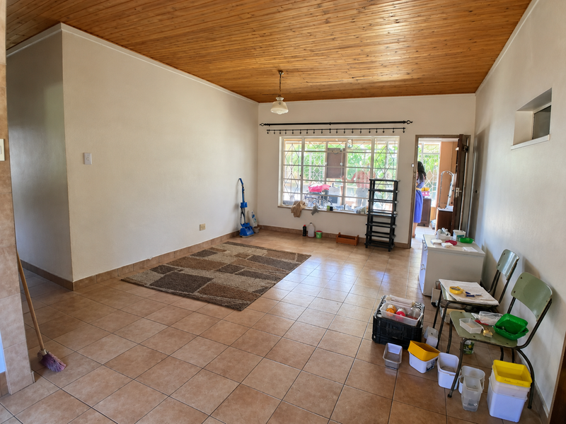 Spacious living area featuring a timber-clad ceiling, ceramic tiled flooring, and large windows with security bars, offering a blank canvas for interior design.